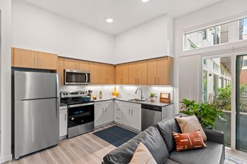A living room with a couch and a kitchen with stainless steel appliances